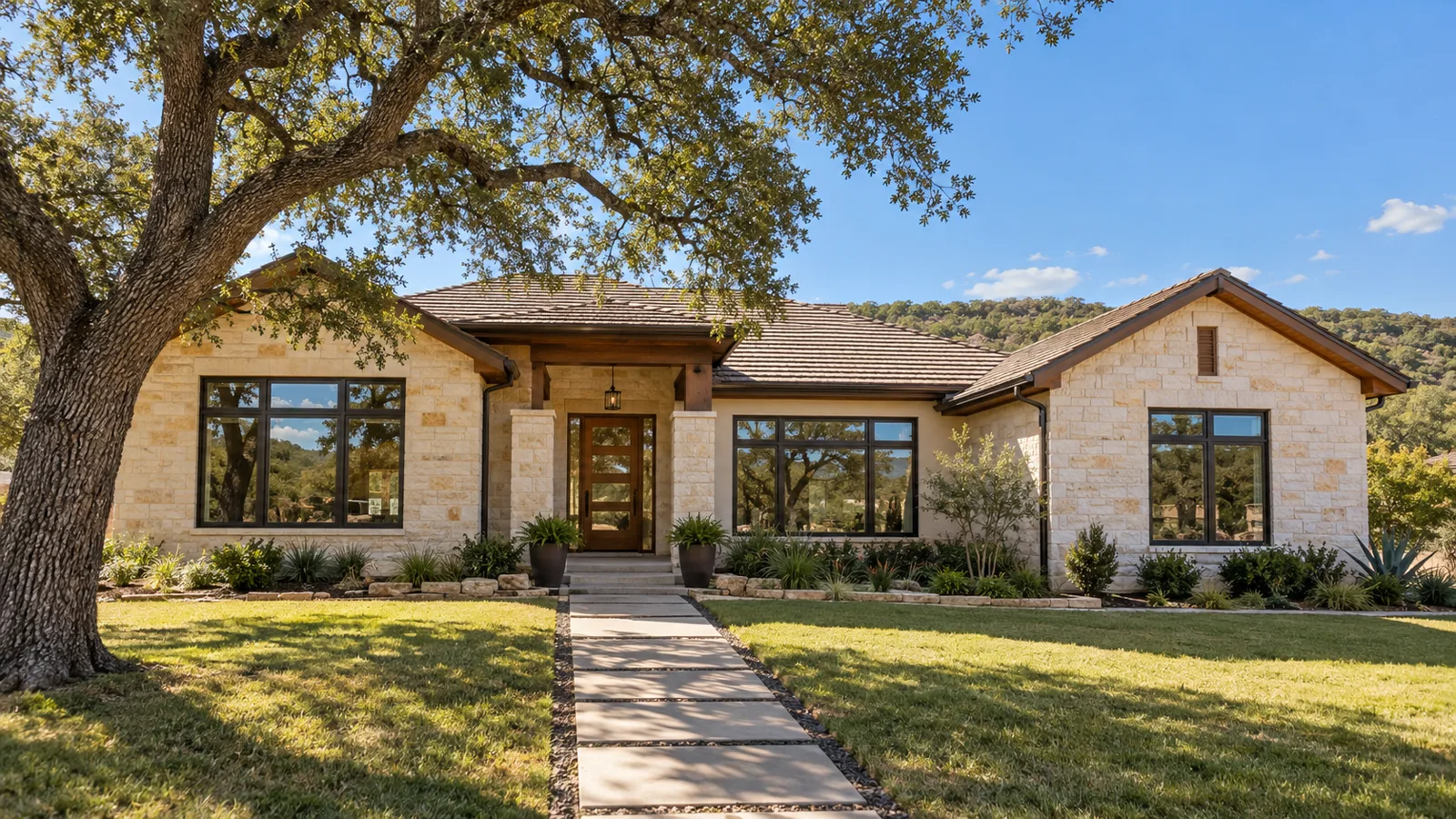 A single-storey Austin Hill Country limestone home with new dark bronze replacement windows, a live oak and a stone path to the front door