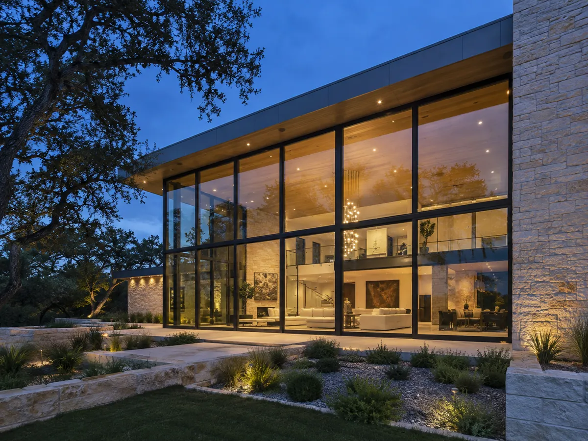 A two-storey fixed glass wall on a modern home, lit from inside at dusk