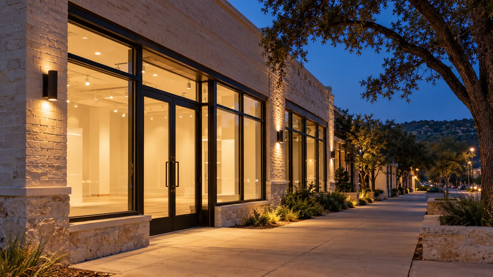 New aluminum storefront glass and double entry doors on a small limestone retail building in Austin at dusk